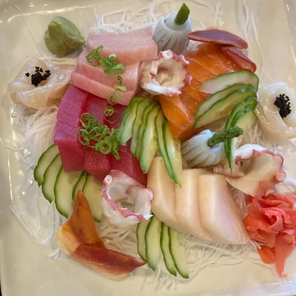 A vibrant sashimi platter with various fish, octopus, scallops, cucumbers, and ginger on a white plate.