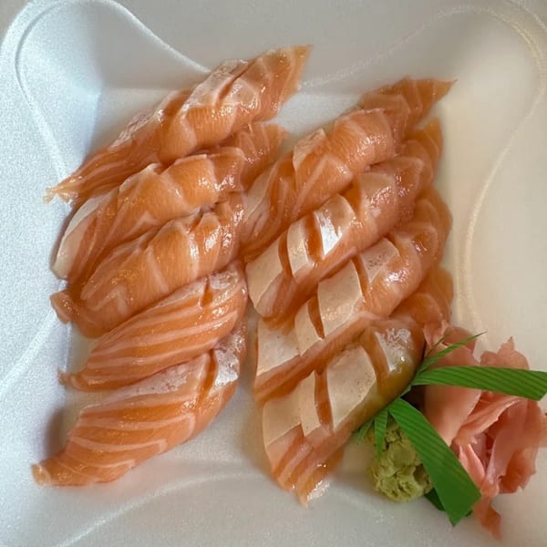 Fresh salmon sashimi with wasabi and pickled ginger in a white takeout container.