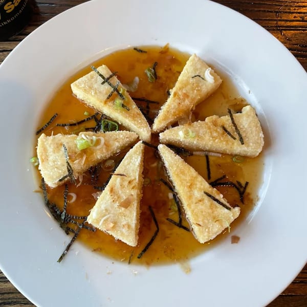 Agedashi Tofu, triangular fried tofu pieces in a savory broth, garnished with seaweed and scallions.