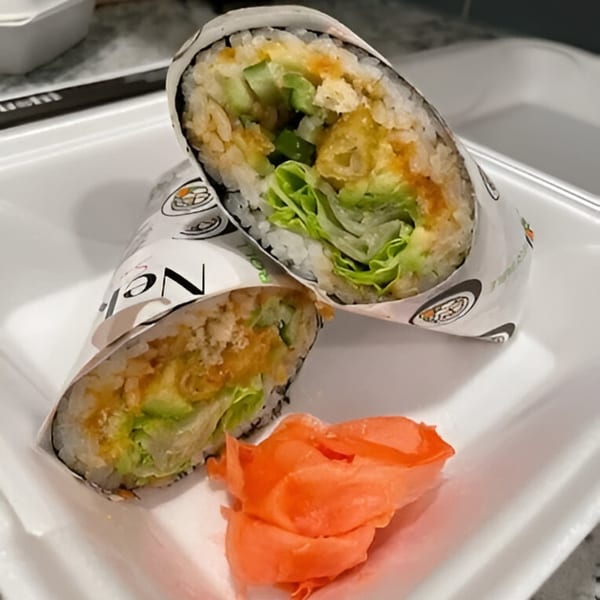 Two halves of a sushi burrito with rice, lettuce, and tempura, alongside pickled ginger.